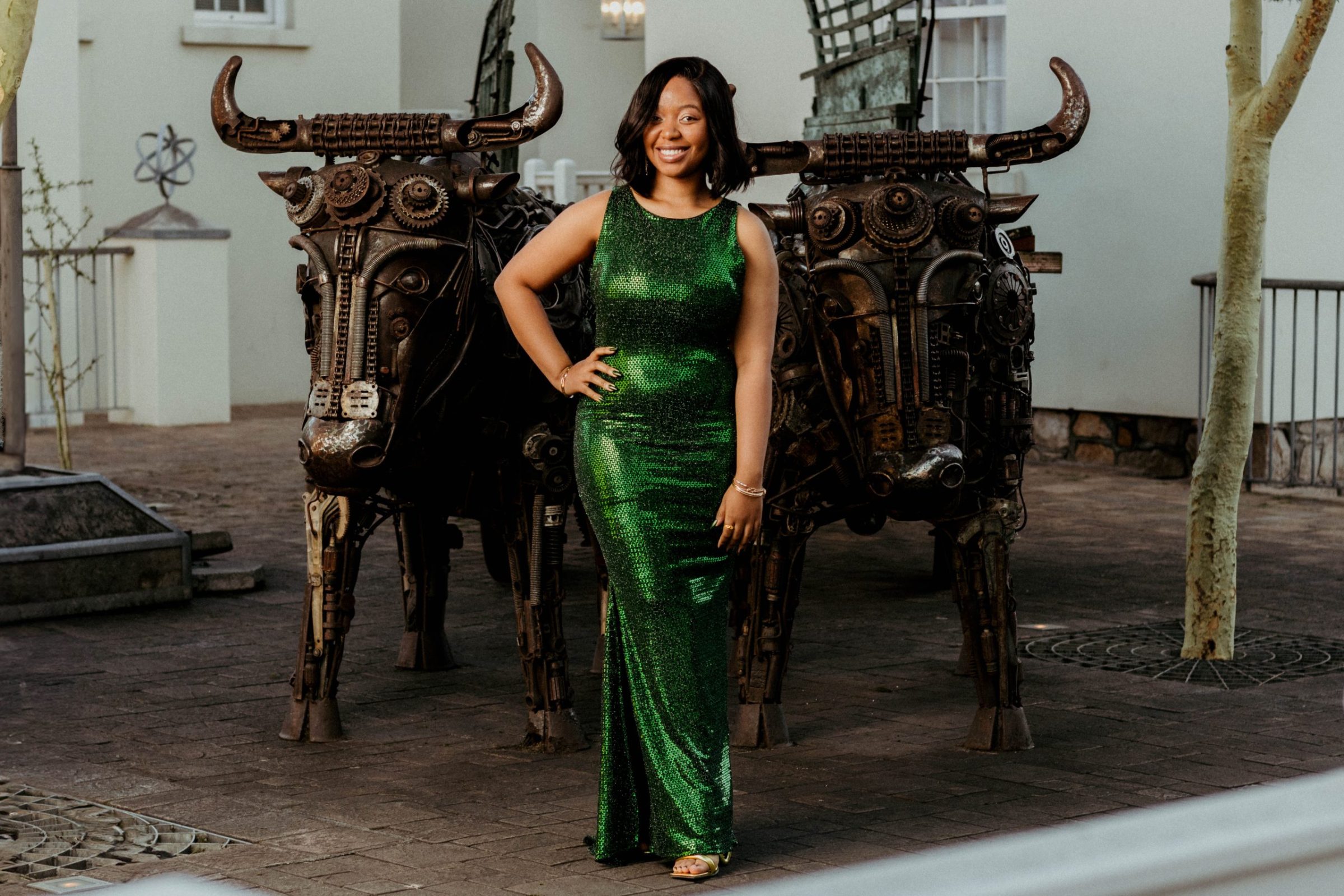 Matriculant woman posing in a green evening dress in front of metal welded bull statues.