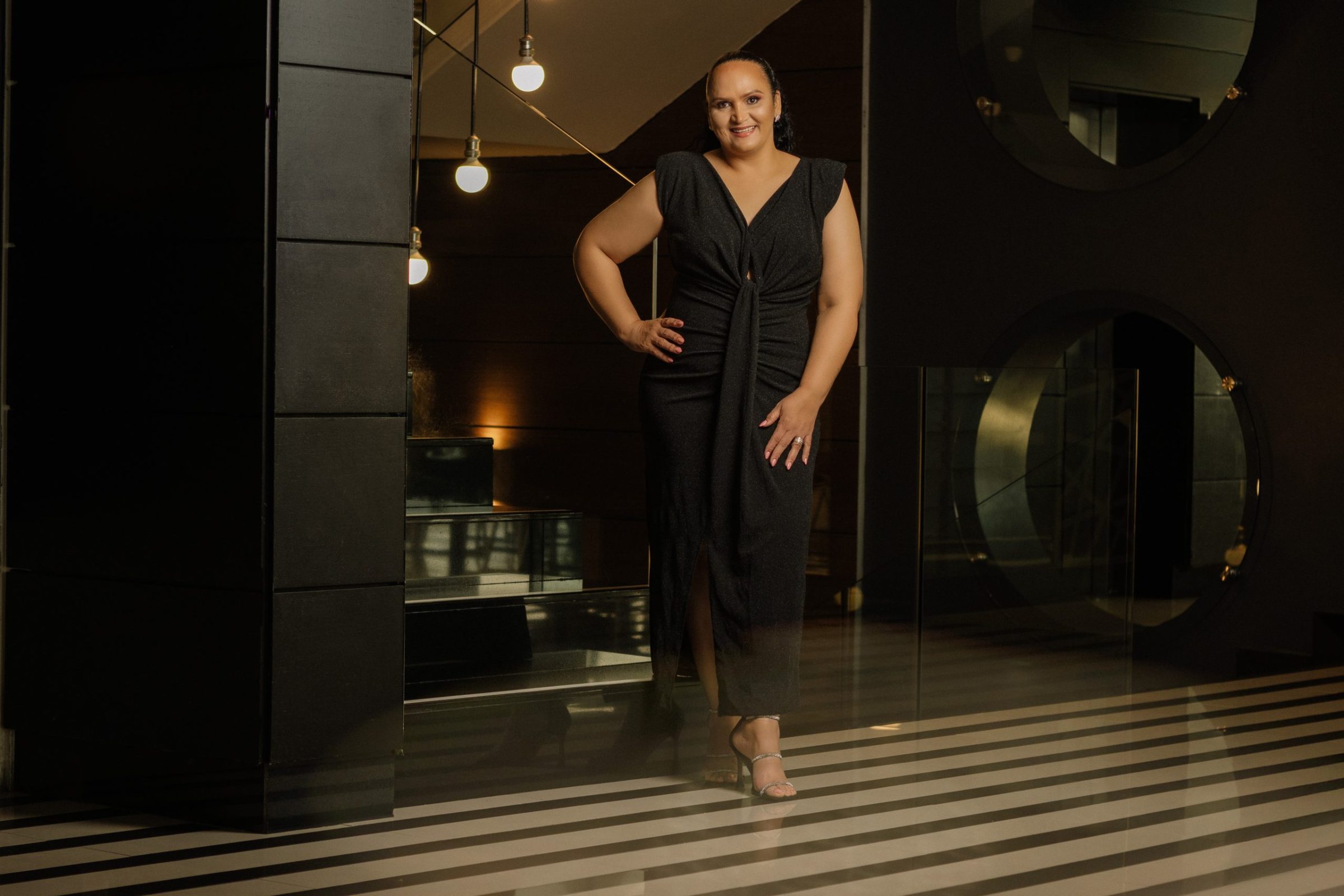 Woman dressed in black dress standing at the stairs, posing in the Hotel lobby for a photo